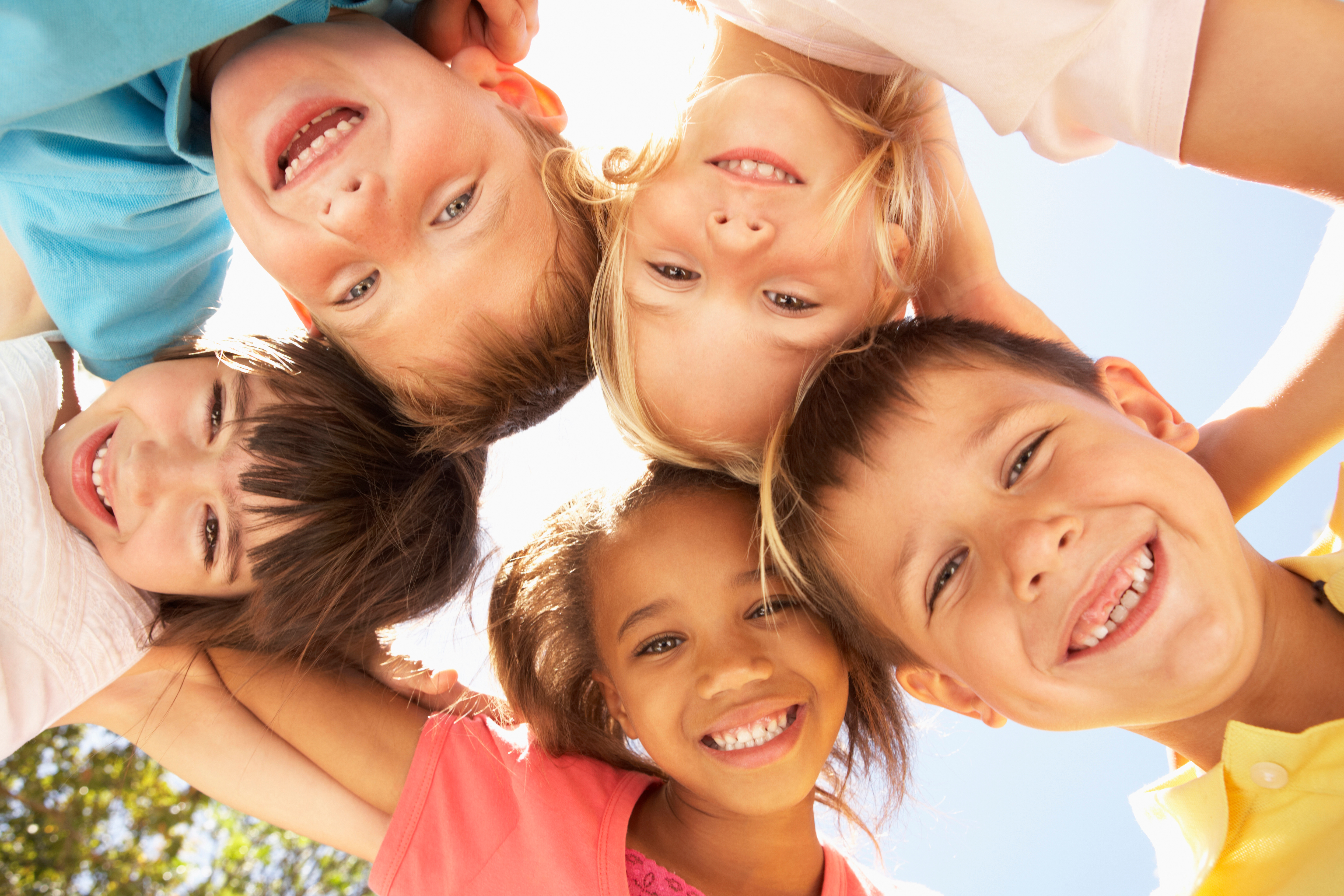 fünf Kinder, die von oben im Kreis und sich umarmend in die Kamera schauen
